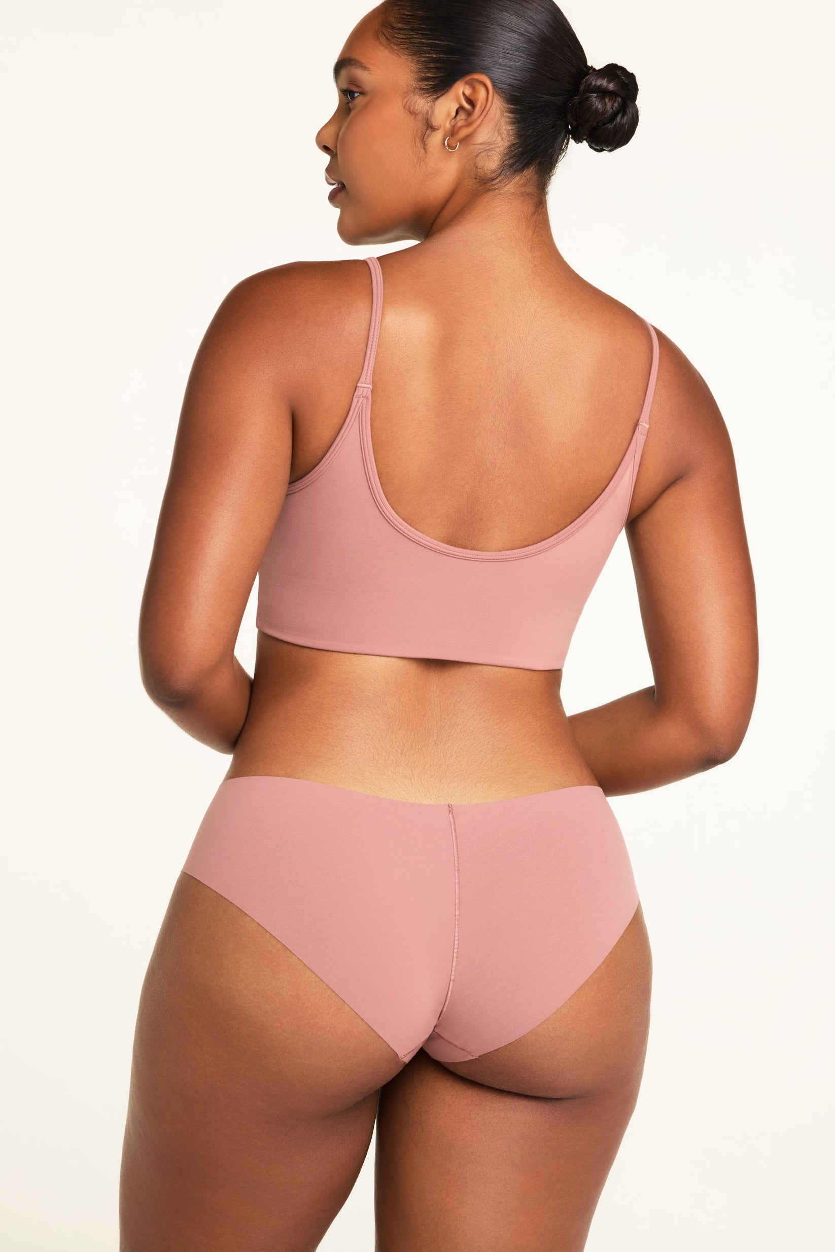 On a white studio backdrop, Amber wears the WhippedKnit Scoop and No-Show Hiphugger in Plum, shown from the back to highlight the Scoop’s straps and Hiphugger coverage.