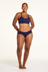 On a white studio backdrop, Amber wears the WhippedKnit V-Neck and No-Show Hiphugger in Noir, shown in a full-length front view.