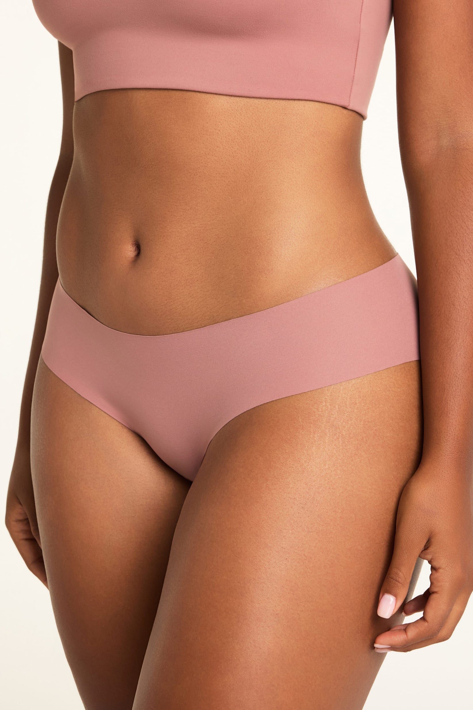 On a white studio backdrop, close-up of Amber wearing the WhippedKnit Scoop and No-Show Hiphugger in Plum, showing the smooth, low-profile underwear fabric.