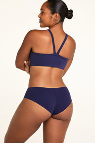 On a white studio backdrop, Amber wears the WhippedKnit V-Neck and No-Show Hiphugger in Noir from the back, showing the back of the bra and underwear.