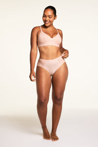 On a light studio backdrop, Amber wears the Bliss Lace Highwaist Brief in Ember Rose, shown in close-up to highlight the soft lace panels and high-waisted design.