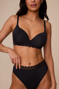 On a neutral studio backdrop, Marcela wears the Base Lace T-Shirt Bra in Black with matching underwear. The close-up front view highlights the smooth molded cups, underwire support, adjustable straps, and lace detail at the center gore and waistband. sizing: Marcela wears size 32D