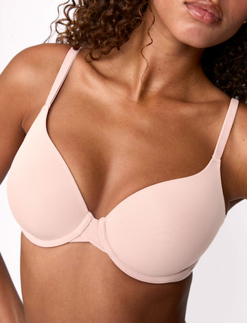 On a light studio backdrop, Courtney wears the Base T-Shirt Bra in Rose, shown in a close-up. The bra features smooth molded cups, a lightly lined design, adjustable straps, and an underwire for support. sizing: Courtney wears size 32D
