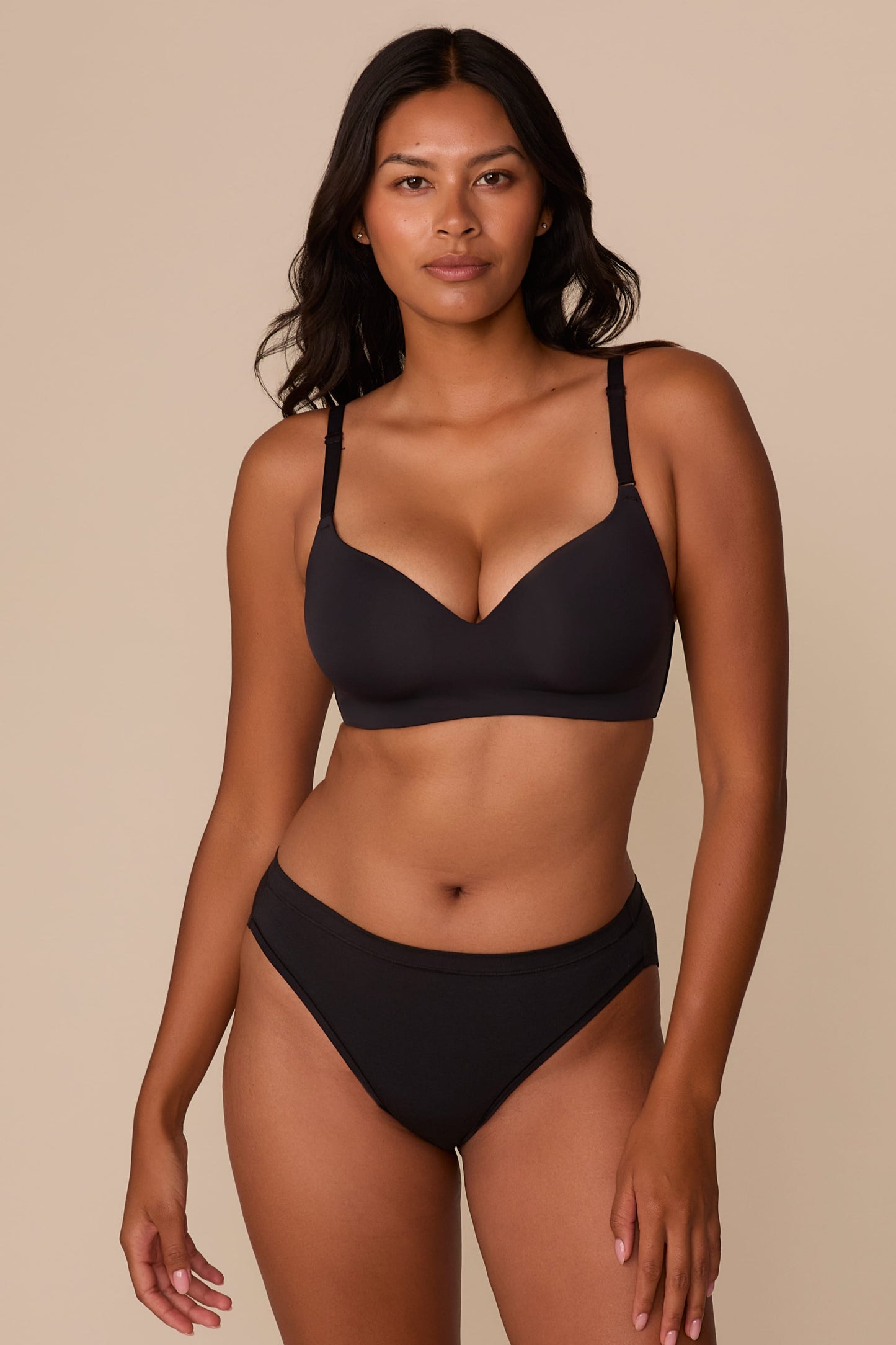 On a neutral beige backdrop, Victoria wears the Base Wirefree T-Shirt Bra in Black with matching underwear, showcasing the smooth molded cups, wireless design, and adjustable straps. sizing: Victoria wears size 32DD