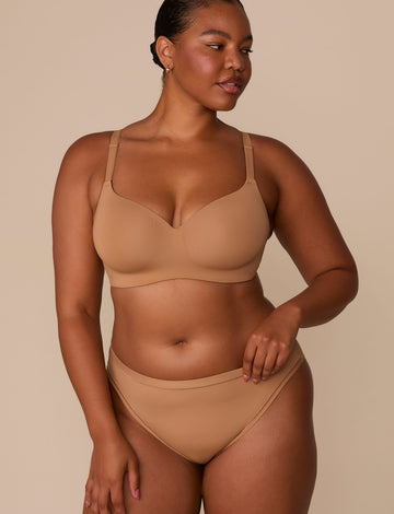 On a neutral beige backdrop, Zarria wears the Base Wirefree T-Shirt Bra in Tan with matching underwear, showcasing the smooth molded cups, wireless design, and adjustable straps.  sizing: Zarria wears size 38D