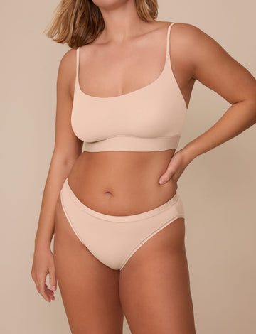On a neutral beige backdrop, Sonnie wears the Bliss Bikini in Beige with a matching Bliss bralette, showing the low-rise silhouette, smooth fabric, and soft waistband.  sizing: Sonnie wears size Large