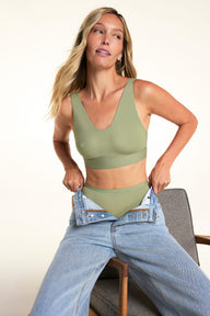 In a bright studio, Meagan wears the Bliss Bralette in Dill with matching underwear while pulling on light-wash jeans. The wireless bralette features a V-neckline, wide straps, and a smooth microfiber finish. sizing: Meagan wears size Small


