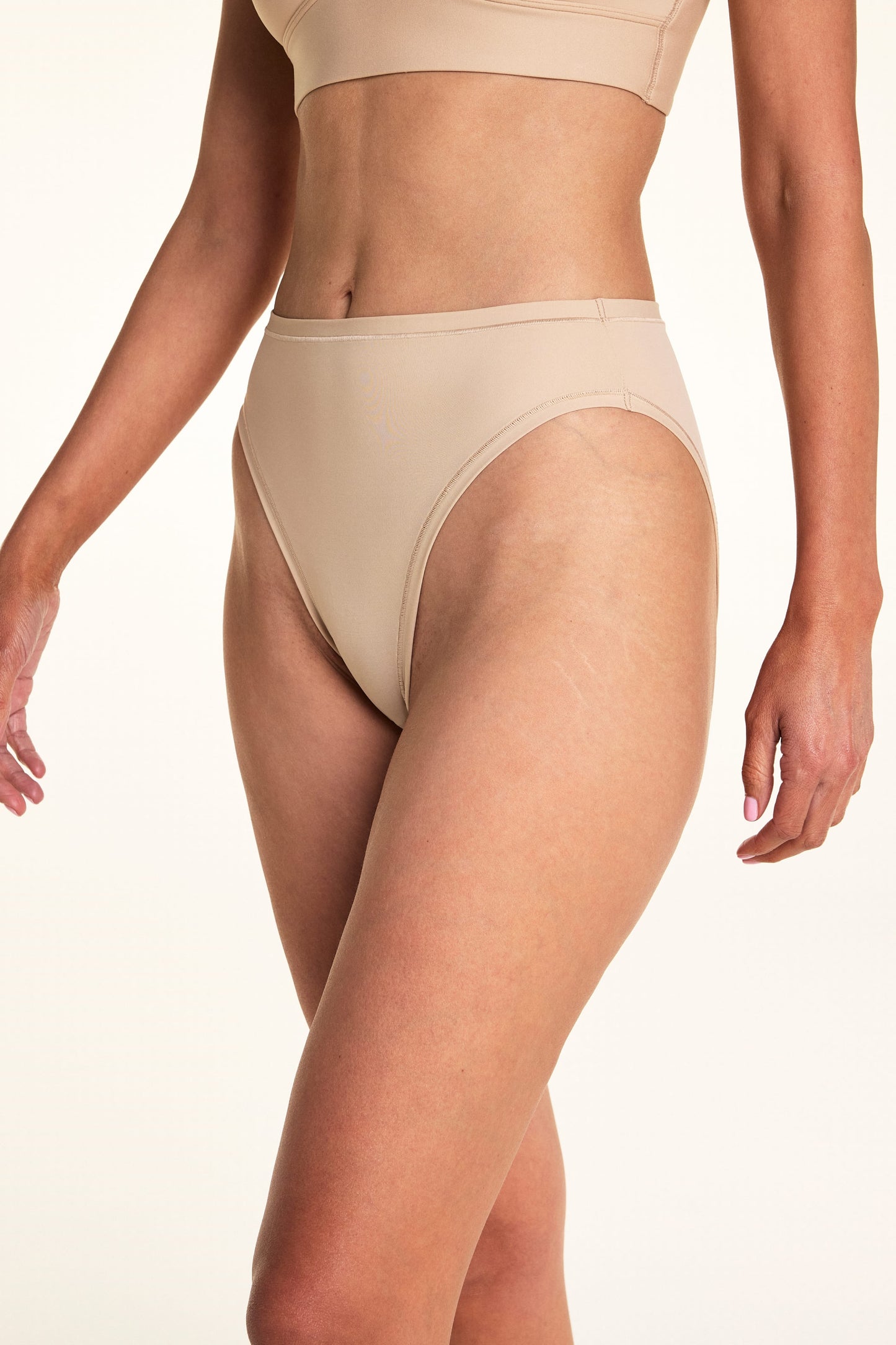 Against a white studio backdrop, Meagan wears the Bliss French Cut underwear in Beige, showing the high-cut leg openings and smooth fabric in a close-up front-facing pose. sizing: Meagan wears size Medium