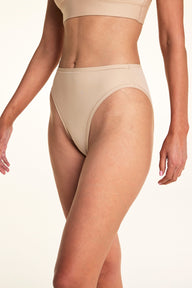 Against a white studio backdrop, Meagan wears the Bliss French Cut underwear in Beige, showing the high-cut leg openings and smooth fabric in a close-up front-facing pose. sizing: Meagan wears size Medium