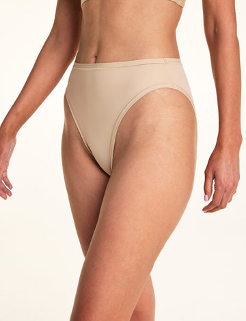Against a white studio backdrop, Meagan wears the Bliss French Cut underwear in Beige, showing the high-cut leg openings and smooth fabric in a close-up front-facing pose. sizing: Meagan wears size Medium