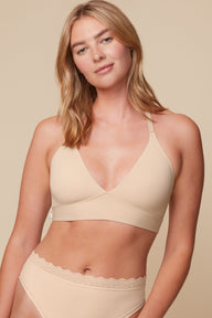On a neutral beige backdrop, Megan wears the Bliss Lace Halterneck Bralette in Beige with matching underwear, showcasing the deep V-neckline, smooth cups, and wide comfort band. sizing: Megan wears size Medium