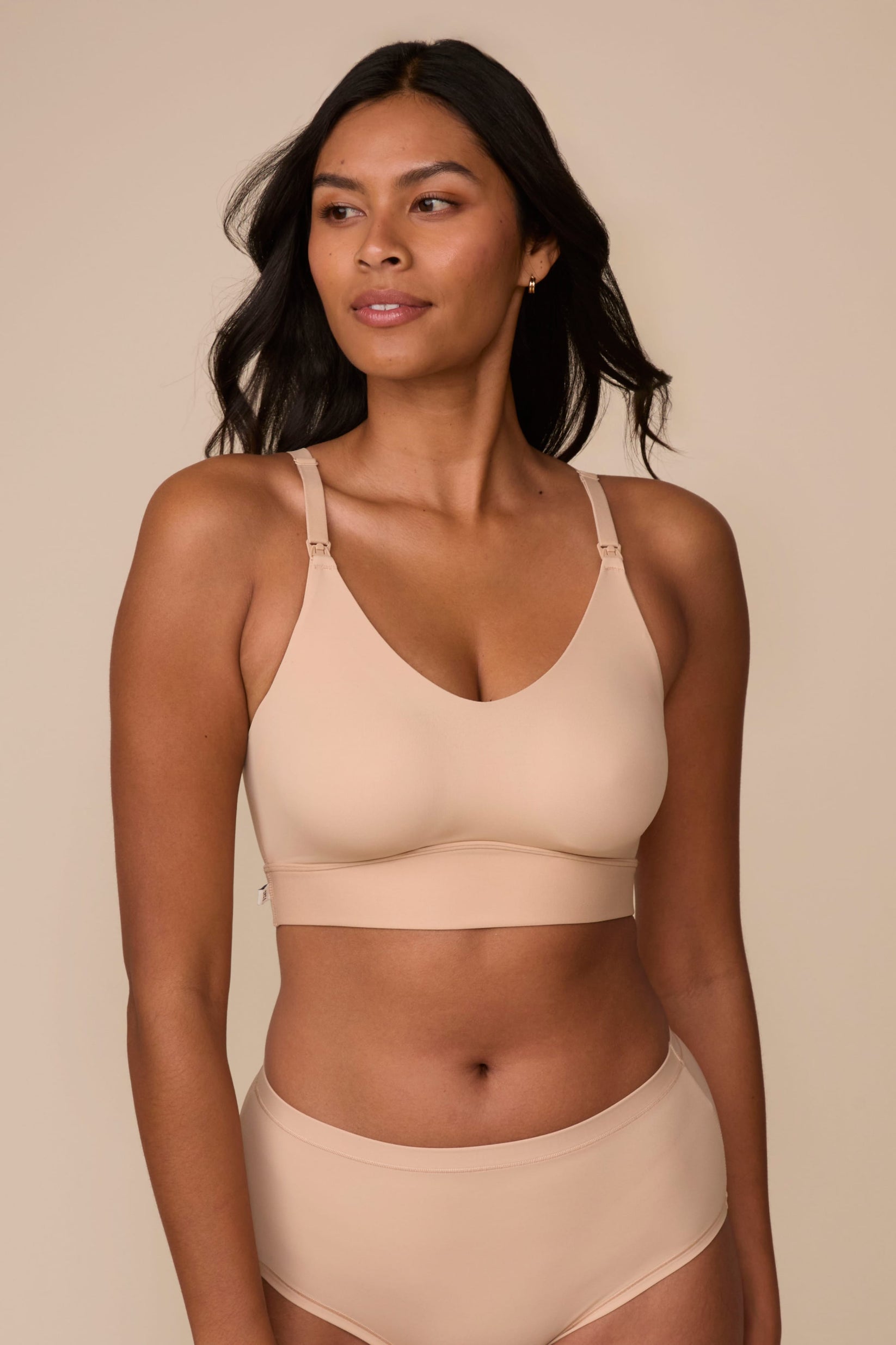 On a neutral studio backdrop, Victoria wears the Bliss Nursing Bralette in Beige with matching underwear. She looks to the side, highlighting the smooth fabric, wireless design, nursing clips at the straps, and supportive underband. sizing: Victoria wears size Medium
