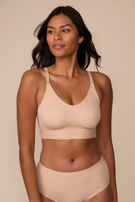 On a neutral studio backdrop, Victoria wears the Bliss Nursing Bralette in Beige with matching underwear. She looks to the side, highlighting the smooth fabric, wireless design, nursing clips at the straps, and supportive underband. sizing: Victoria wears size Medium