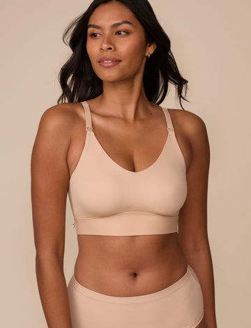 On a neutral studio backdrop, Victoria wears the Bliss Nursing Bralette in Beige with matching underwear. She looks to the side, highlighting the smooth fabric, wireless design, nursing clips at the straps, and supportive underband. sizing: Victoria wears size Medium