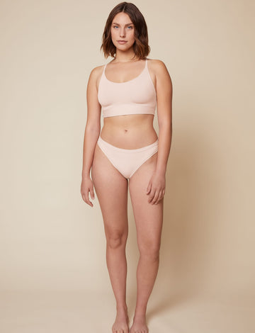 On a neutral beige backdrop, Carli wears the Bliss Racerback Bralette in Rose with coordinating underwear, showcasing the scoop neckline, adjustable straps, and supportive underband in a full-body front view.  sizing: Carli wears size Medium