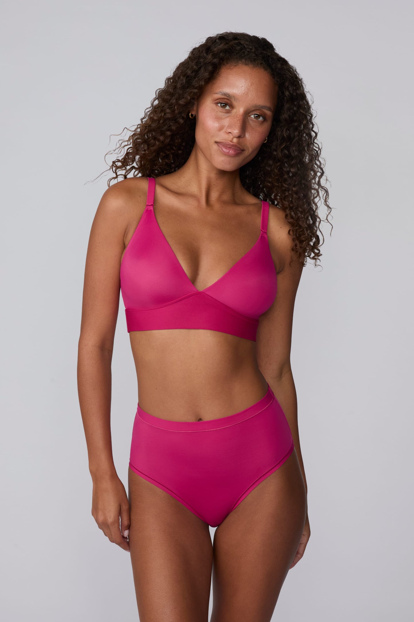 On a light gray studio backdrop, Courtney wears the Bliss Triangle Bralette in Winterberry with matching underwear. The front-facing view highlights the deep V-neckline, smooth molded cups, adjustable straps, and wide underband for comfortable support. sizing: Courtney wears size Small