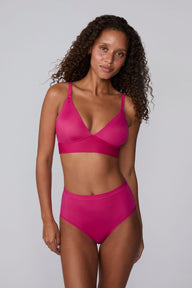 On a light gray studio backdrop, Courtney wears the Bliss Triangle Bralette in Winterberry with matching underwear. The front-facing view highlights the deep V-neckline, smooth molded cups, adjustable straps, and wide underband for comfortable support. sizing: Courtney wears size Small