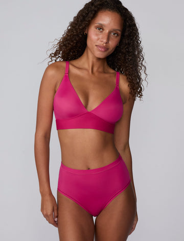On a light gray studio backdrop, Courtney wears the Bliss Triangle Bralette in Winterberry with matching underwear. The front-facing view highlights the deep V-neckline, smooth molded cups, adjustable straps, and wide underband for comfortable support. sizing: Courtney wears size Small