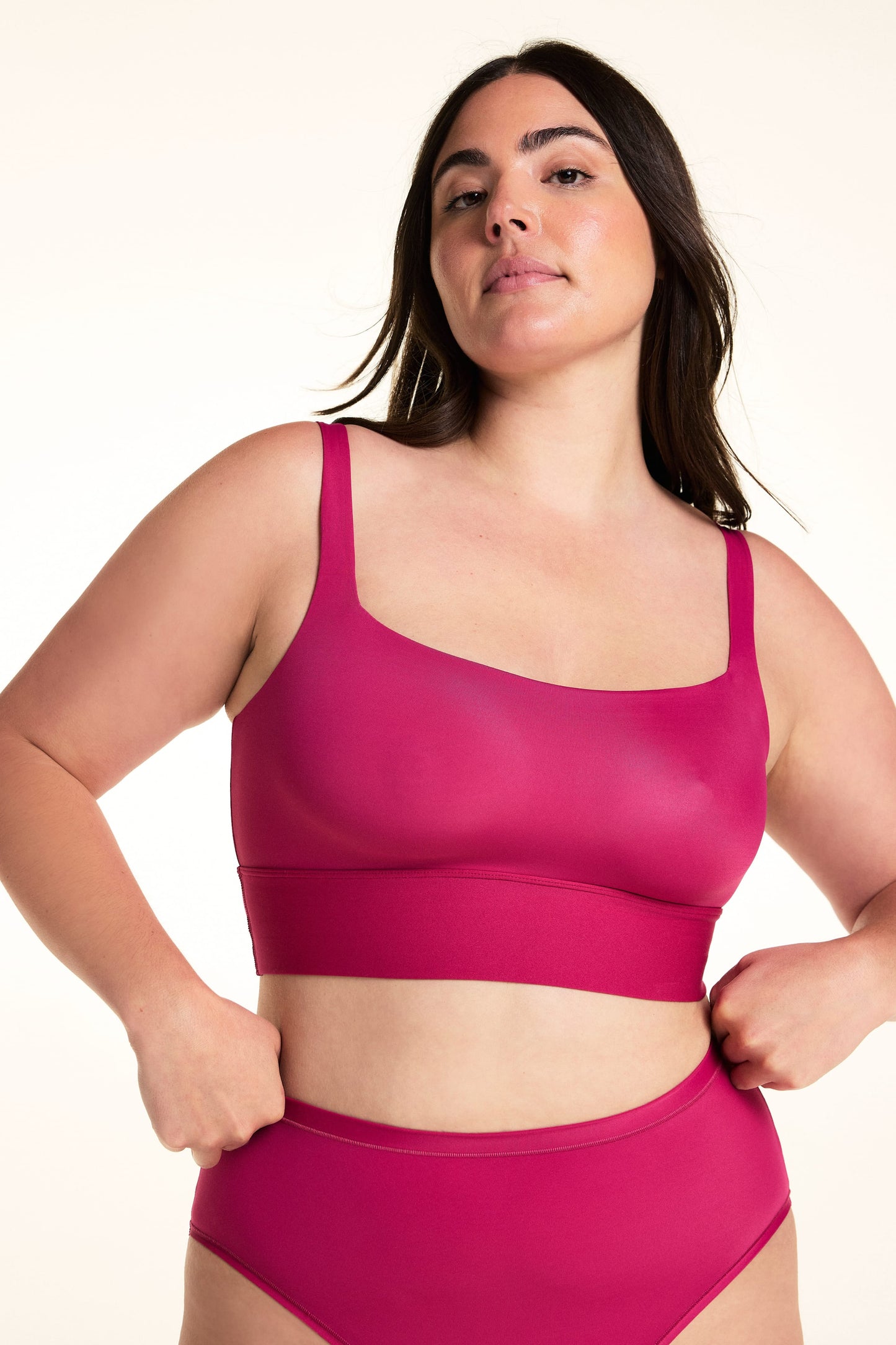 On a light studio backdrop, Alessandra wears the Bliss Square Neck Bralette in Winterberry. The front view highlights the square neckline, wide comfort band, smooth fabric, and supportive straps. sizing: Alessandra wears size Large