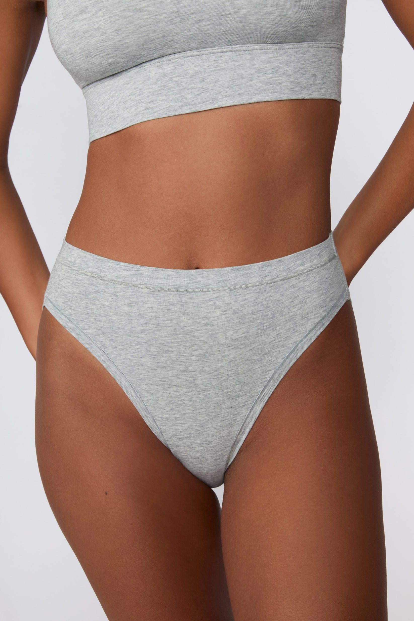 On a light gray studio backdrop, Courtney wears the Cloud Cotton French Cut Brief in Heather Grey. The close-up front view highlights the French-cut leg opening, mid-rise waistband, and soft cotton fabric. sizing: Courtney wears size Small