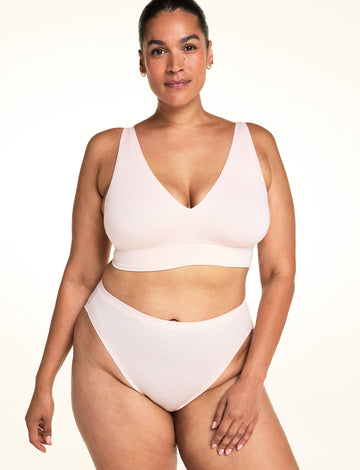 On a light studio backdrop, Jennifer wears the Cloud Cotton French Cut in Dogwood with the Bliss Triangle Bralette in Dogwood. The image highlights the high-cut leg opening, smooth waistband, and soft cotton fabric. sizing: Jennifer wears size Large