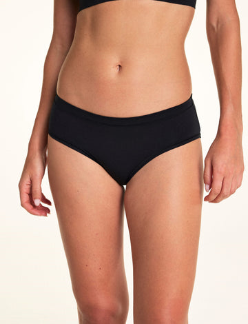 Against a neutral studio backdrop, Alexis wears the Cloud Cotton Hiphugger underwear in Black, featuring a low-rise silhouette, soft waistband, and everyday coverage. sizing: Alexis wears size Small