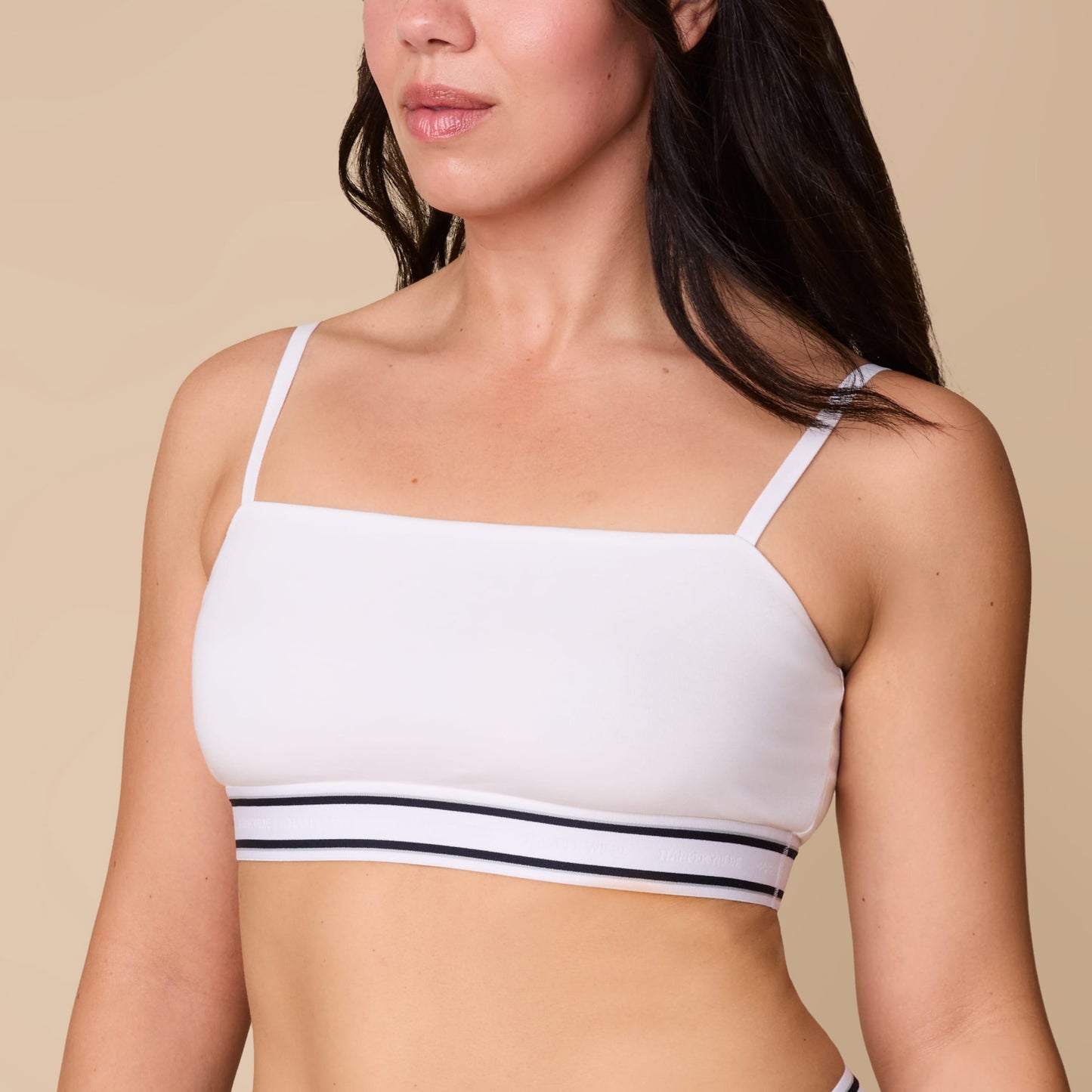 On a neutral beige backdrop, Emersyn wears the Cloud Cotton Retro Bandeau Bralette in White with matching underwear, showcasing the straight neckline, slim adjustable straps, and striped elastic underband.