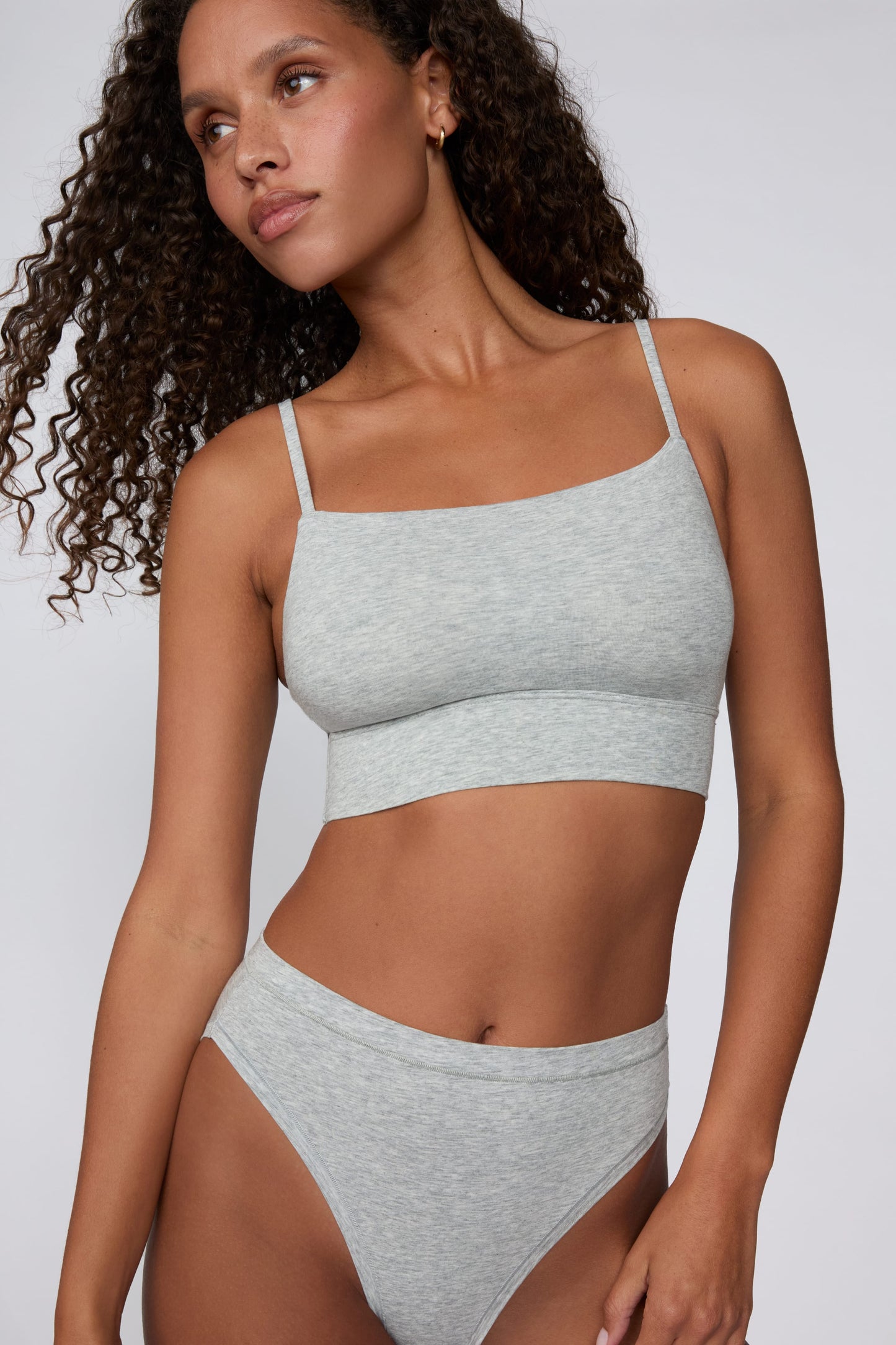 On a light gray studio backdrop, Courtney wears the Cloud Cotton Thin Strap Bralette in Heather Grey with matching underwear. The front view highlights the straight neckline, thin adjustable straps, soft cotton fabric, and wide underband. sizing: Courtney wears size Small