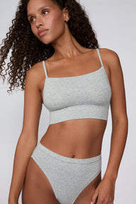 On a light gray studio backdrop, Courtney wears the Cloud Cotton Thin Strap Bralette in Heather Grey with matching underwear. The front view highlights the straight neckline, thin adjustable straps, soft cotton fabric, and wide underband. sizing: Courtney wears size Small