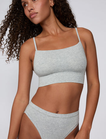 On a light gray studio backdrop, Courtney wears the Cloud Cotton Thin Strap Bralette in Heather Grey with matching underwear. The front view highlights the straight neckline, thin adjustable straps, soft cotton fabric, and wide underband. sizing: Courtney wears size Small