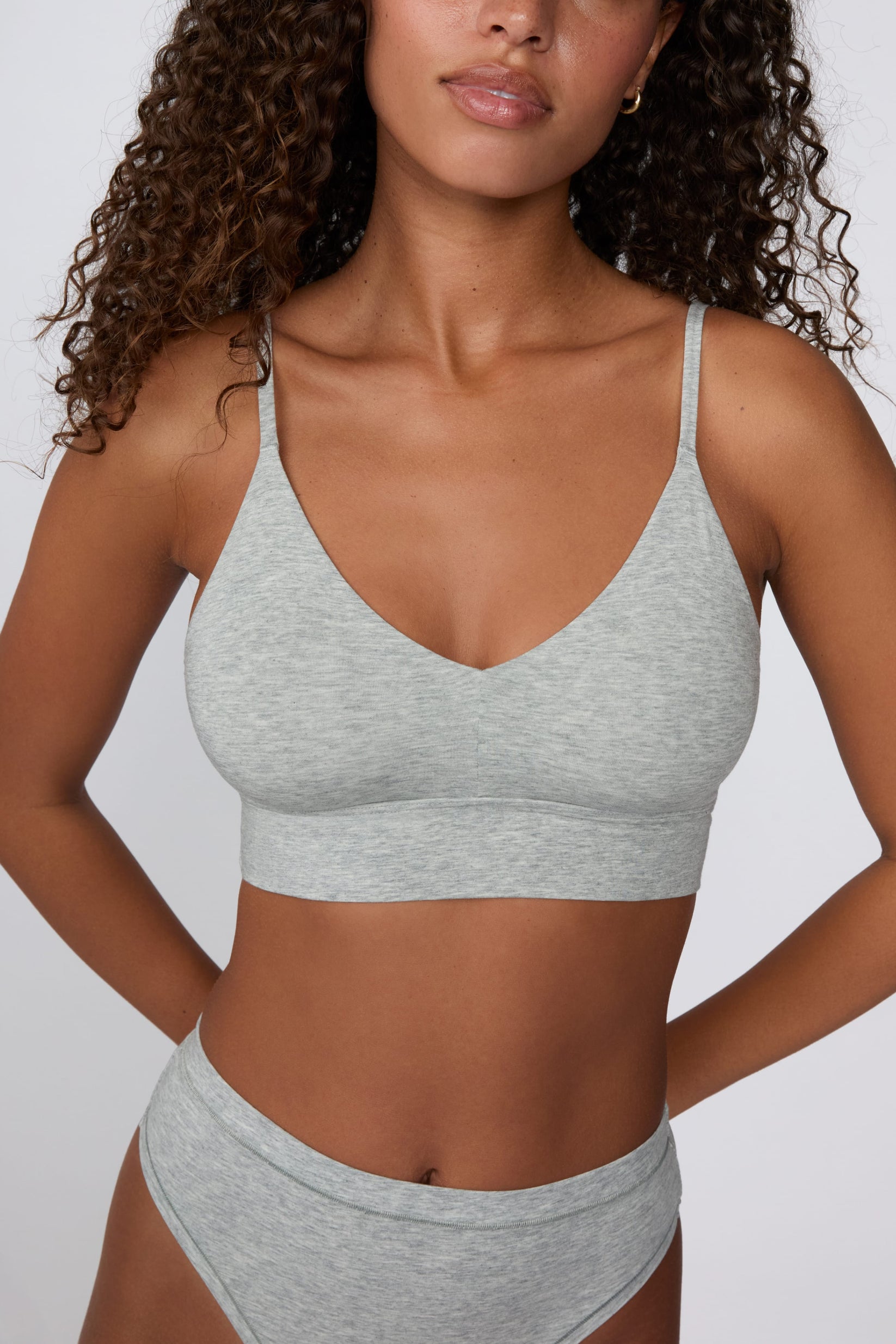 On a light gray studio backdrop, Courtney wears the Cloud Cotton Triangle Bralette in Heather Grey with matching underwear. The close-up front view highlights the soft cotton fabric, deep V-neckline, and thin adjustable straps. sizing: Courtney wears size Small
