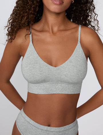 On a light gray studio backdrop, Courtney wears the Cloud Cotton Triangle Bralette in Heather Grey with matching underwear. The close-up front view highlights the soft cotton fabric, deep V-neckline, and thin adjustable straps. sizing: Courtney wears size Small
