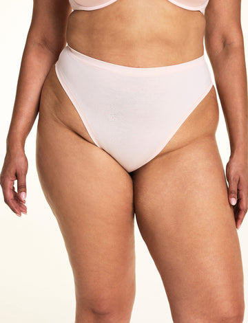 On a light studio backdrop, Jennifer wears the Cloud Cotton Highwaist Thong in Dogwood. The close-up highlights the high-rise waistband, high-cut leg opening, and soft cotton fabric. sizing: Jennifer wears size XL