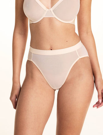 On a light studio backdrop, Laura wears the ComfortMesh™ Plunge Bra and ComfortMesh™ Highwaist Brief in Pearl. The high-rise brief features soft sheer mesh fabric, a wide waistband, and moderate back coverage. 