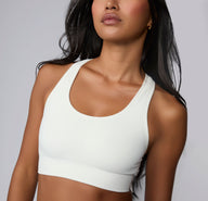On a light gray studio backdrop, Amber wears the Seamless Racerback Sports Bra in White, shown from the front to highlight the smooth scoop neckline, knit-in support panels, and wide underband. The soft, seamless fabric is shown up close for comfortable, low-impact support. sizing: Amber wears size XS