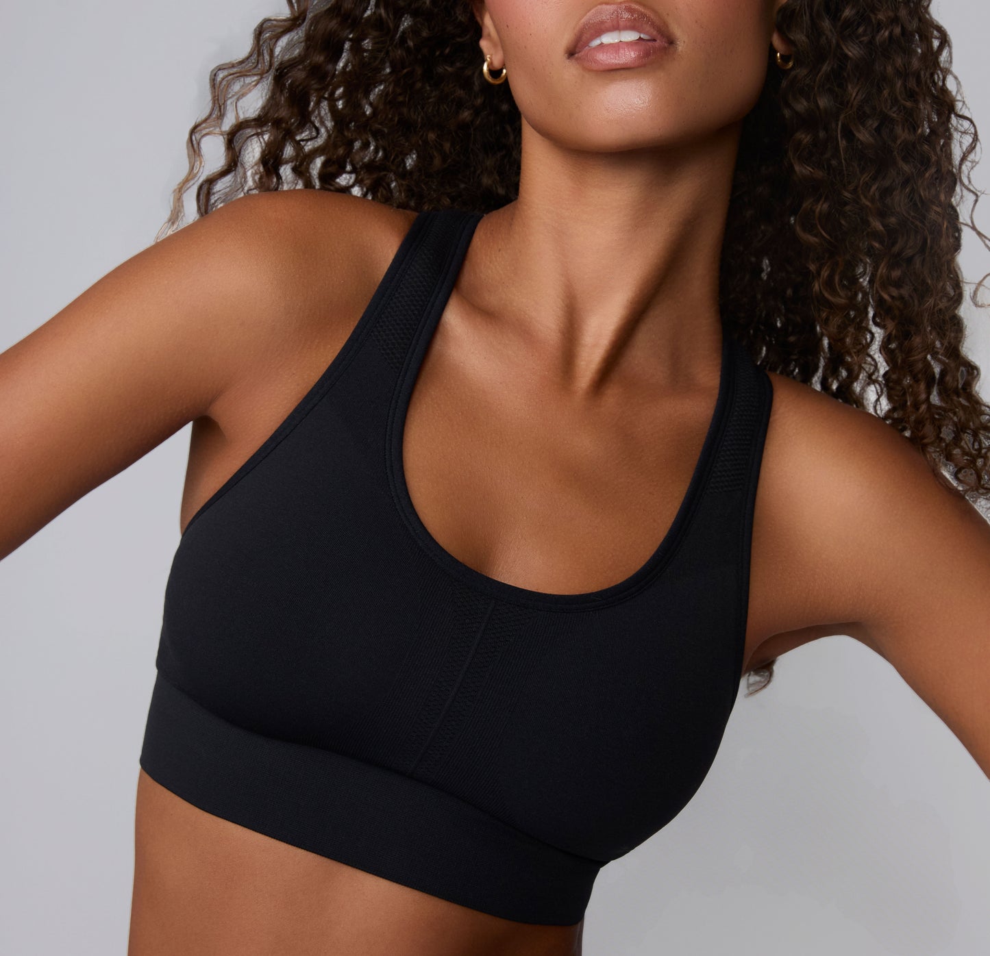 On a neutral studio backdrop, Courtney is shown in a close-up front angle wearing the Seamless Racerback Sports Bra in Black. The smooth scoop neckline, wireless support, and wide underband are visible. sizing: Courtney wears size Small