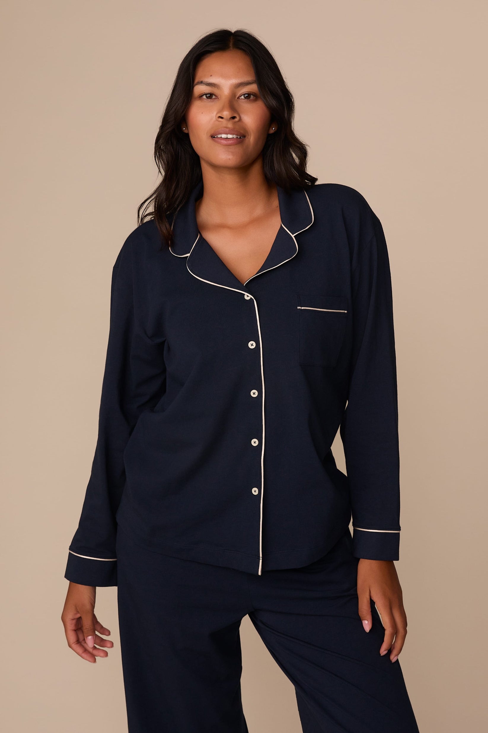 On a neutral studio backdrop, Victoria wears the Perfect Pima Pajama Long Sleeve Shirt in Navy with matching pajama pants. The front view highlights the relaxed fit, button-front closure, chest pocket, and contrast piping along the collar, placket, pocket, and cuffs. sizing: Victoria wears size Medium