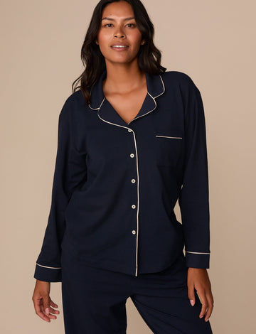 On a neutral studio backdrop, Victoria wears the Perfect Pima Pajama Long Sleeve Shirt in Navy with matching pajama pants. The front view highlights the relaxed fit, button-front closure, chest pocket, and contrast piping along the collar, placket, pocket, and cuffs. sizing: Victoria wears size Medium