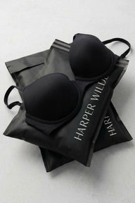 Two black Harper Wilde bras laid on branded black recycling bags — the Recycle, Bra Kit.