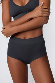 In a studio setting, Courtney wears the Ribbed Seamless Boyshort in Charcoal with a matching ribbed bralette. A close-up view highlights the high-rise waistband, boyshort silhouette, and ribbed texture.  sizing: Courtney wears size Small