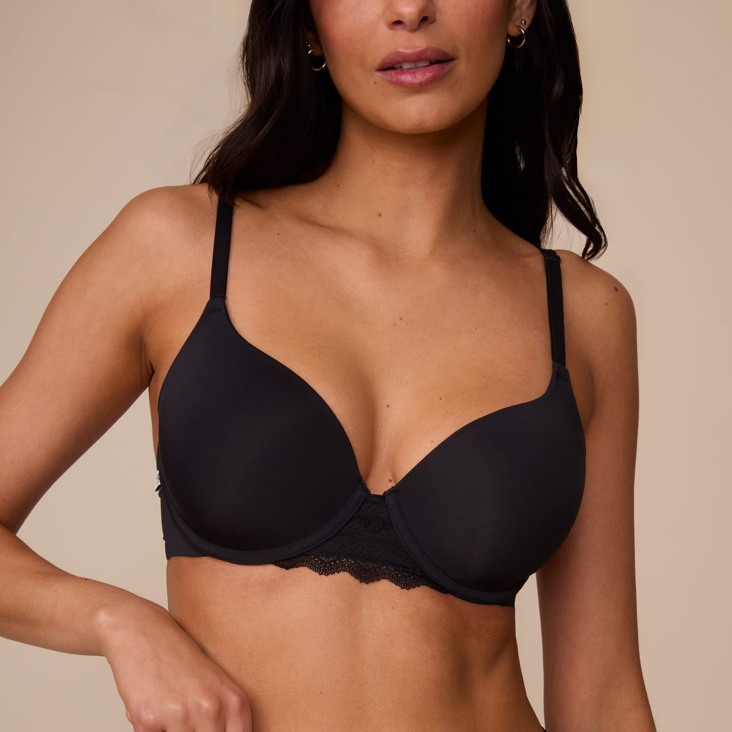 On a neutral studio backdrop, Marcela wears the Base Lace T-Shirt Bra in Black with matching underwear. The close-up front view highlights the smooth molded cups, underwire support, adjustable straps, and lace detail at the center gore and waistband.