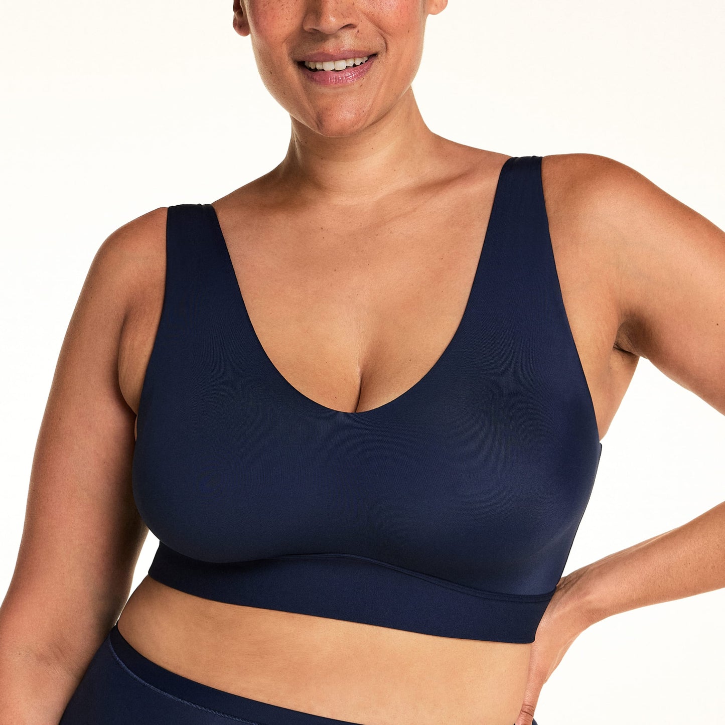 On a light studio backdrop, Jennifer wears the Bliss Bralette in Navy with matching underwear. The cropped image highlights the V-neckline, wide wireless band, and smooth microfiber fabric.