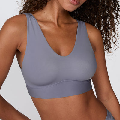 On a white studio backdrop, Courtney wears the Bliss Bralette in Steel, shown in a close-up. The bralette features a deep V-neck, wide straps, and smooth, lightweight fabric.