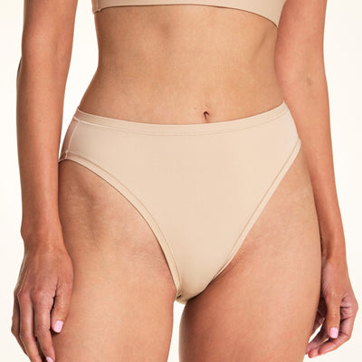 Against a white studio backdrop, Meagan wears the Bliss French Cut underwear in Beige, showing the smooth fabric and high-rise silhouette in a close-up front-facing pose.