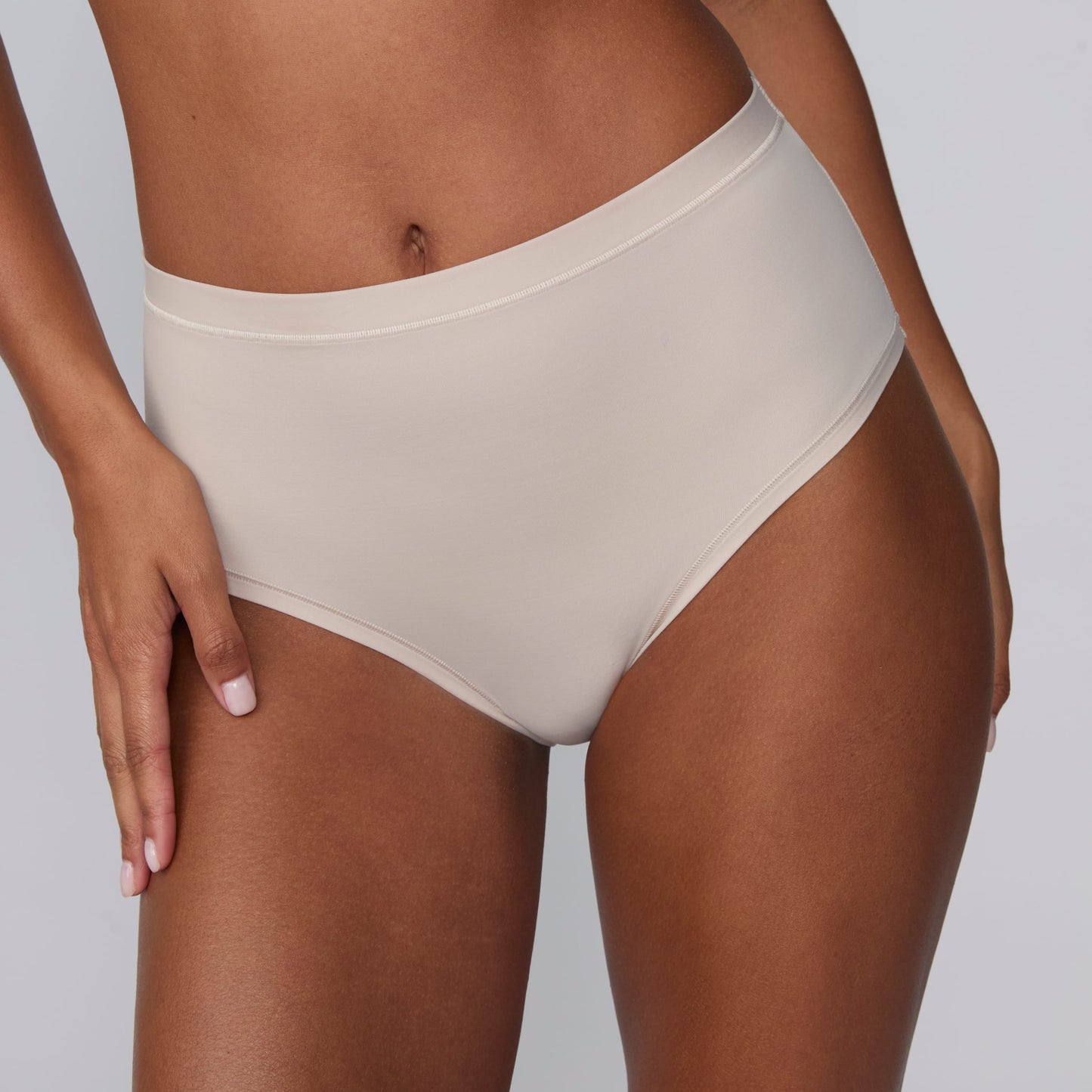 In a studio setting, Courtney wears the Bliss Highwaist Brief in Pebble. A close-up front view highlights the smooth fabric, high-rise waistband, and full-coverage design.