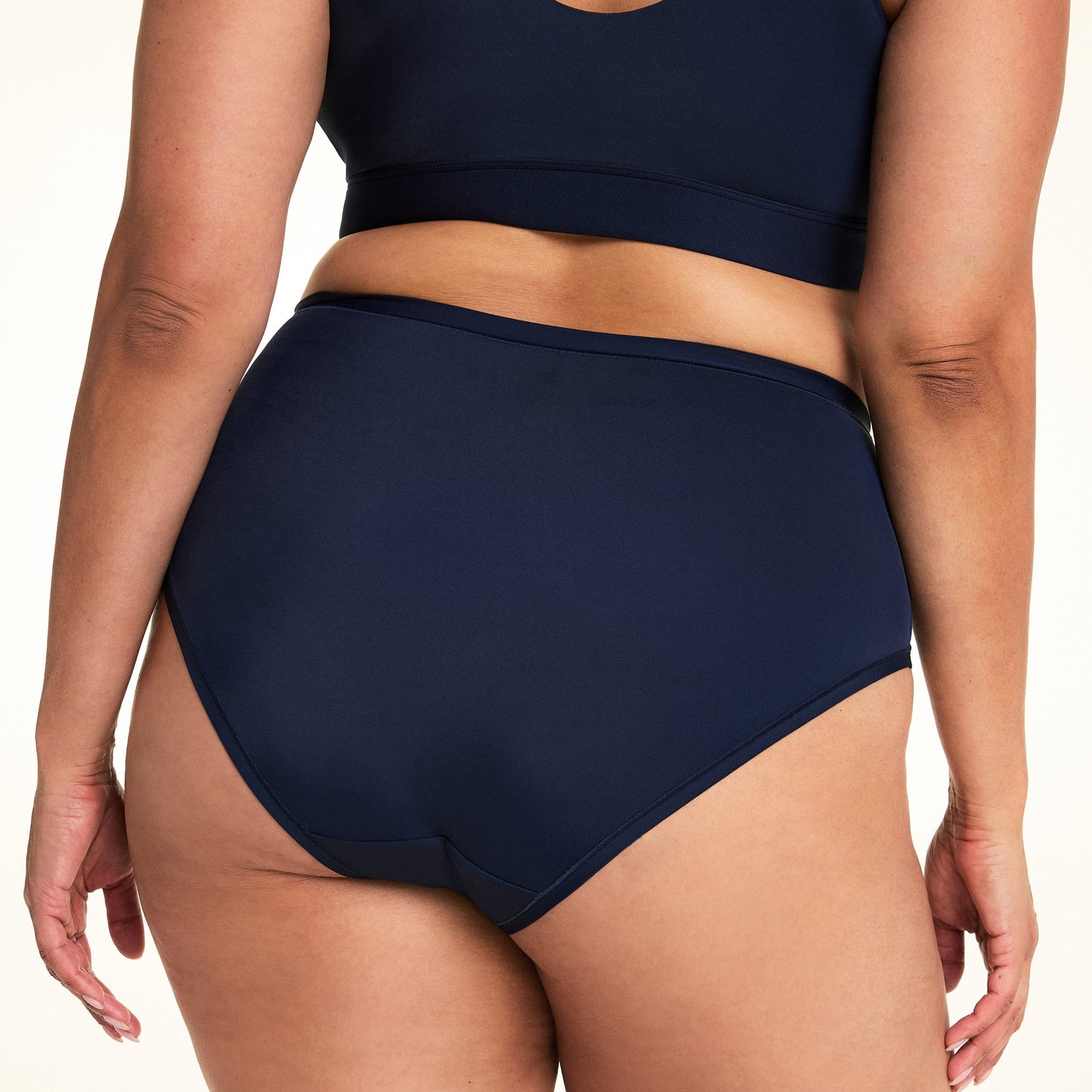 On a light studio backdrop, Jennifer is shown from the back wearing the Bliss Highwaist in Navy. The cropped image highlights the full-coverage back, smooth fabric, and clean finish along the leg openings.q