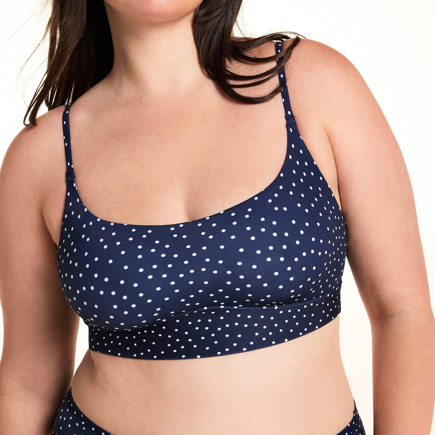 On a light studio backdrop, Alessandra wears the Bliss Scoop Bralette in Navy Dot with matching Navy Dot underwear. The cropped image highlights the scoop neckline, adjustable straps, wide underband, and allover white dot print.