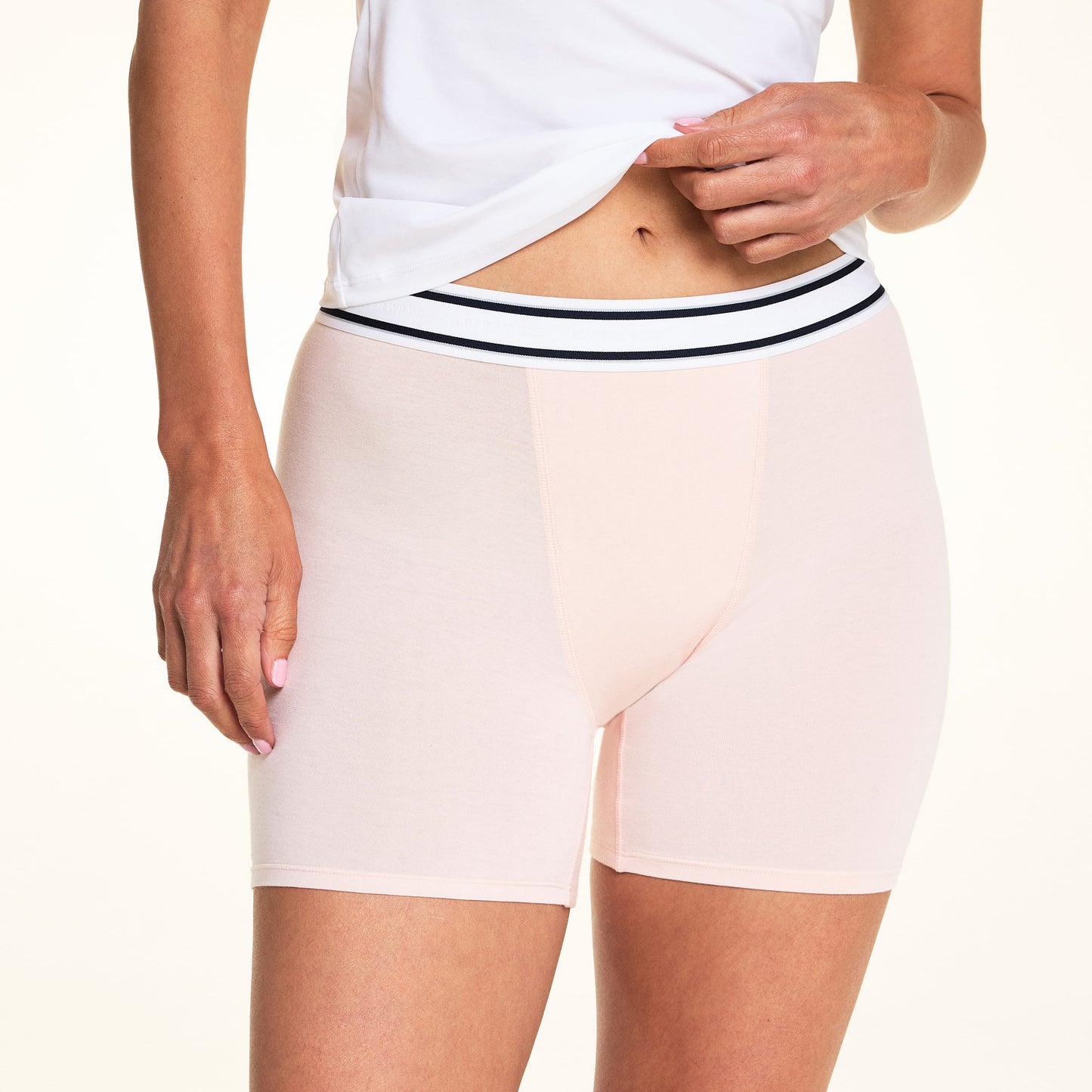 On a light studio backdrop, Meagan wears the Cloud Cotton Boxer Brief in Dogwood with a white tank top. The cropped image highlights the striped elastic waistband, mid-rise fit, and smooth, soft fabric.