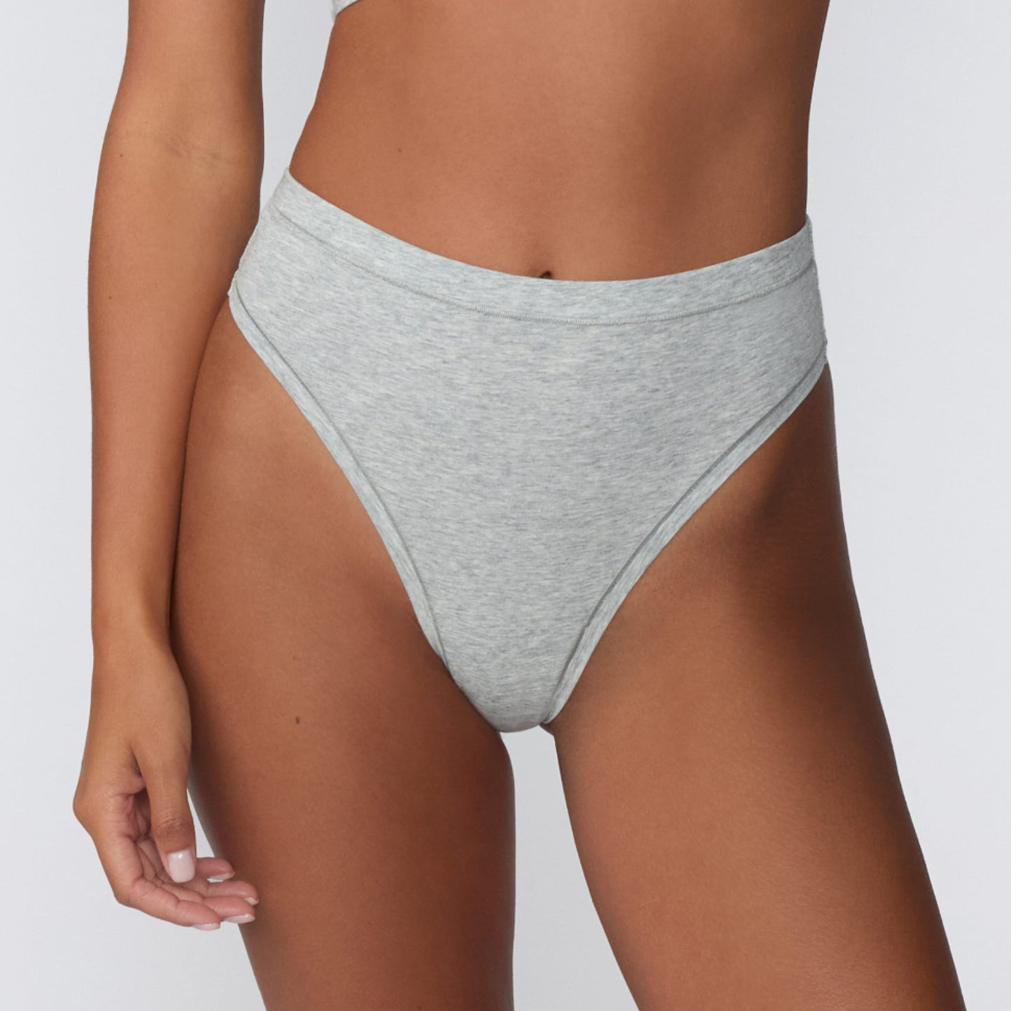 On a light gray studio backdrop, Courtney wears the Cloud Cotton Highwaist Thong in Heather Grey. The close-up front view highlights the high-rise waistband, high-leg cut, and soft cotton fabric.