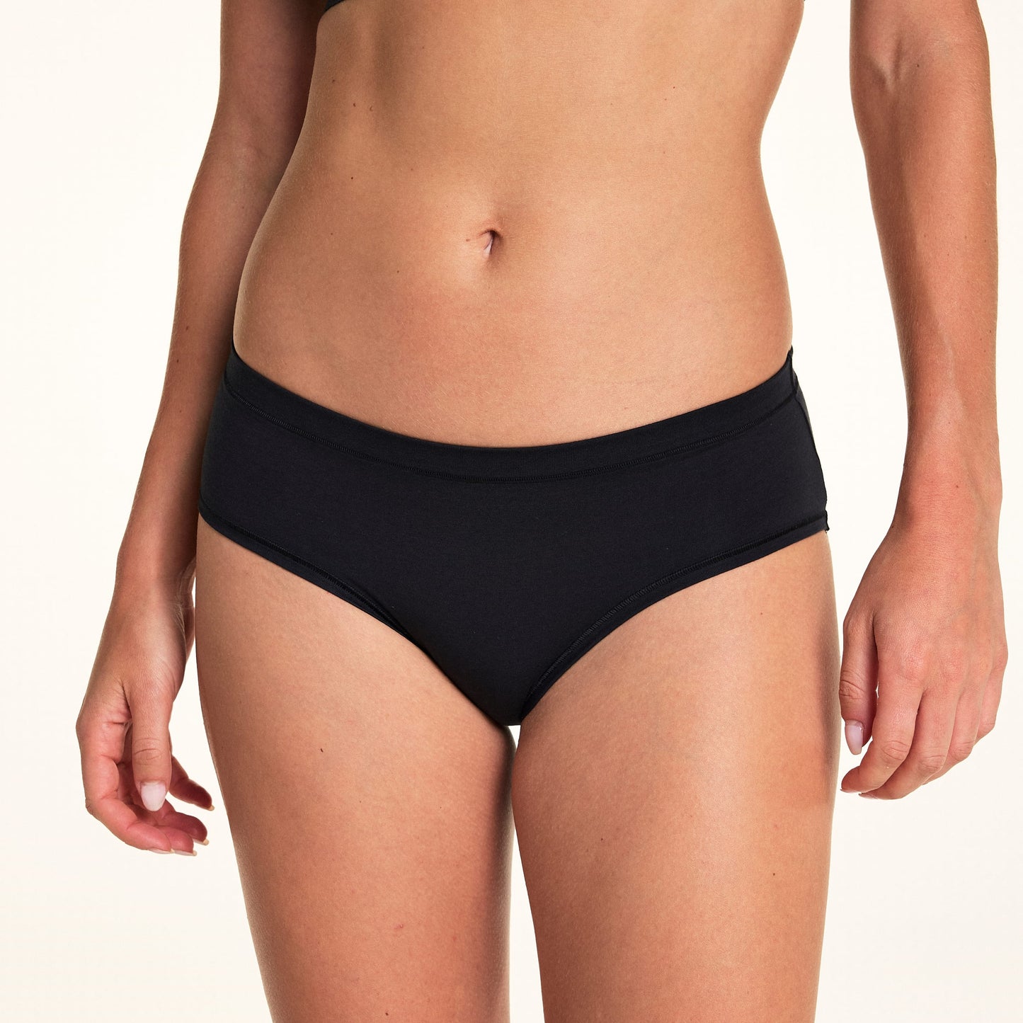 In a close-up studio shot, Alexis wears the Cloud Cotton Hiphugger underwear in Black, featuring smooth edges, a low-rise waistband, and soft cotton fabric.